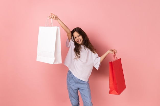 Menina adorável feliz segurando sacolas de papel de compras animadas com descontos de shopping boas compras