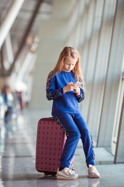 Menina adorável no aeroporto perto de grande janela brincando com seu telefone
