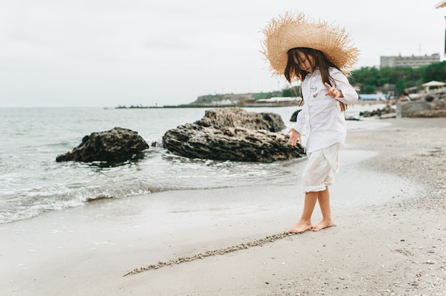 Menina adorável no chapéu de palha na praia durante as férias de verão