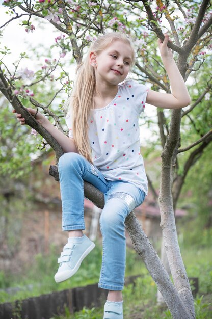 Menina adorável sentada em uma árvore florescendo no jardim de maçãs