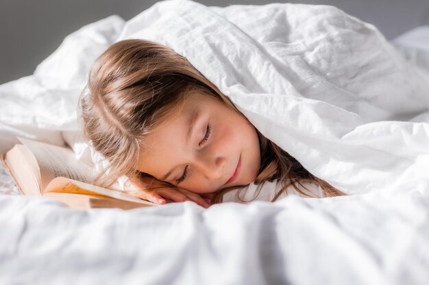 Menina adormeceu com um livro debaixo do cobertor foto de alta qualidade