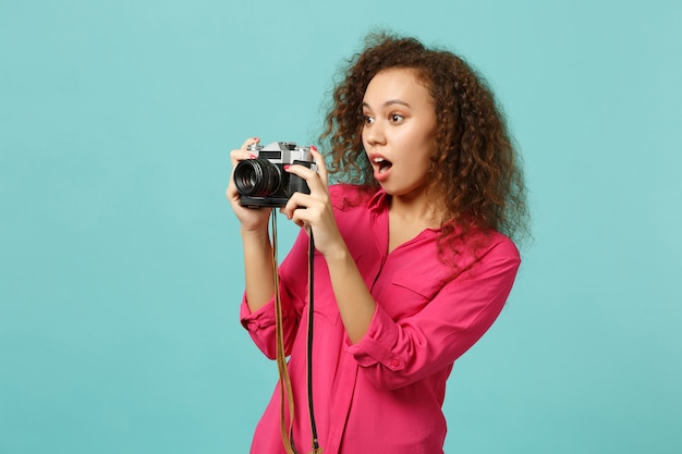 Menina africana chocada em roupas casuais, tirando foto na câmera fotográfica vintage retrô isolada no fundo da parede azul turquesa no estúdio. Conceito de estilo de vida de emoções sinceras de pessoas. Simule o espaço da cópia.