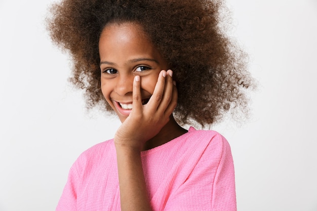 Menina africana divertida alegre usando blusa em pé, isolada na parede branca, fazendo careta, rindo