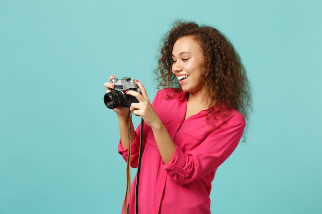 Menina africana sorridente em roupas casuais, tirando foto na câmera fotográfica vintage retrô isolada no fundo da parede azul turquesa no estúdio. Conceito de estilo de vida de emoções sinceras de pessoas. Simule o espaço da cópia.