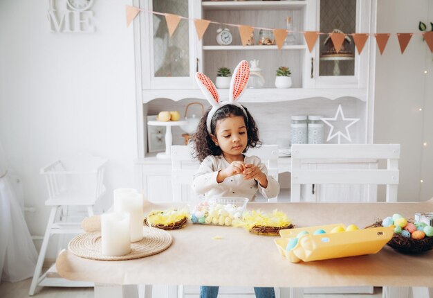 Foto menina afro-americana pinta ovos de páscoa em casa na cozinha feliz páscoa