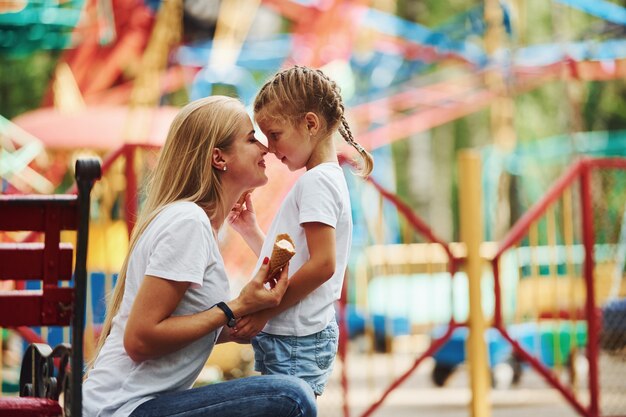 Menina alegre, a mãe dela se divertindo no parque, perto das atrações