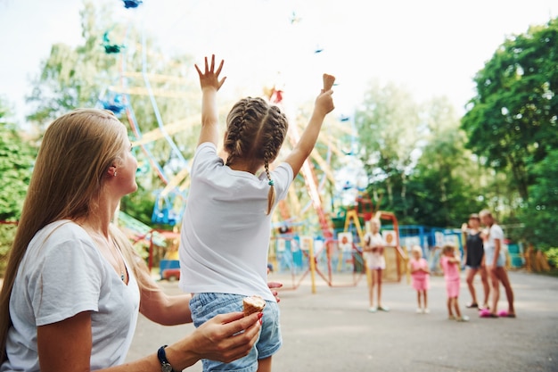 Menina alegre, a mãe dela se divertindo no parque, perto das atrações