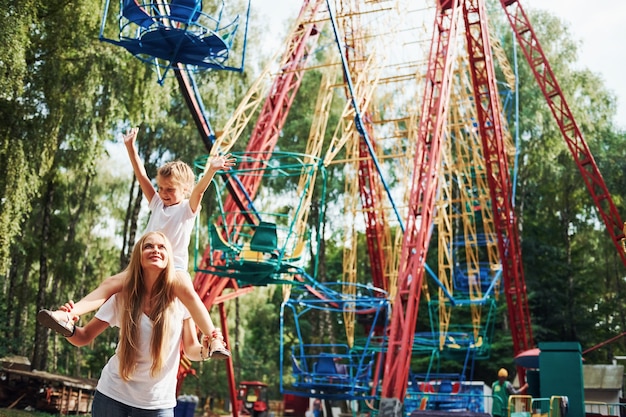 Menina alegre, a mãe dela se divertir no parque juntos, perto de atrações.