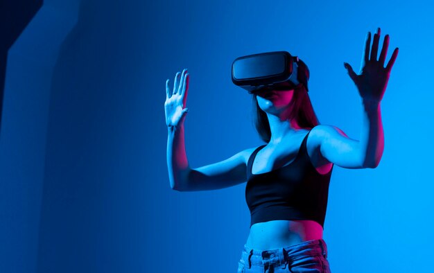 Menina alegre com as mãos para cima usando os óculos de realidade virtual e jogando jogos à luz de néon conceito de tecnologia do futuro Metaverse pessoa