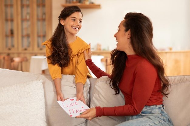 Foto menina alegre com cartão-presente artesanal cumprimentando a mãe em casa