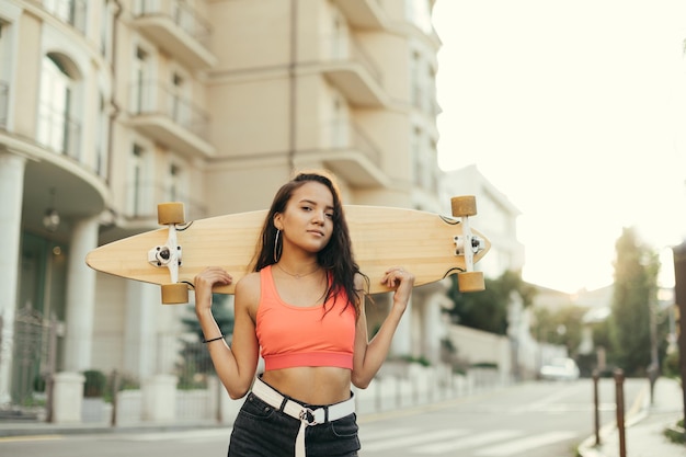 Menina alegre com longboard posando para a câmera copie o espaço