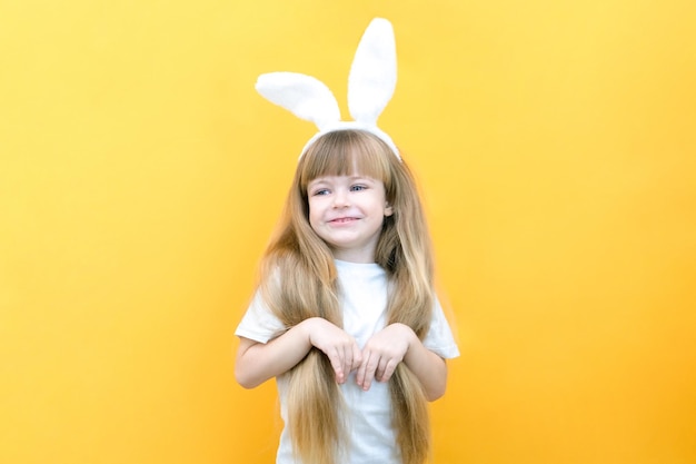 Menina alegre com orelhas de coelho na cabeça em um fundo amarelo Criança feliz louca e engraçada Criança de Páscoa Preparação para os itens promocionais do feriado de Páscoa copiam o espaço para maquete de texto