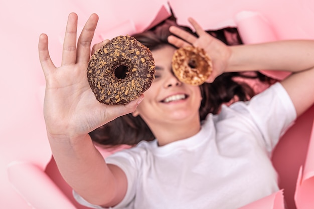 Menina alegre com rosquinhas brilhantes em um fundo de papel rosa