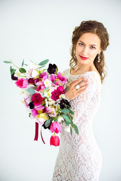 Menina alegre com um vestido de malha branco posando com um buquê de flores