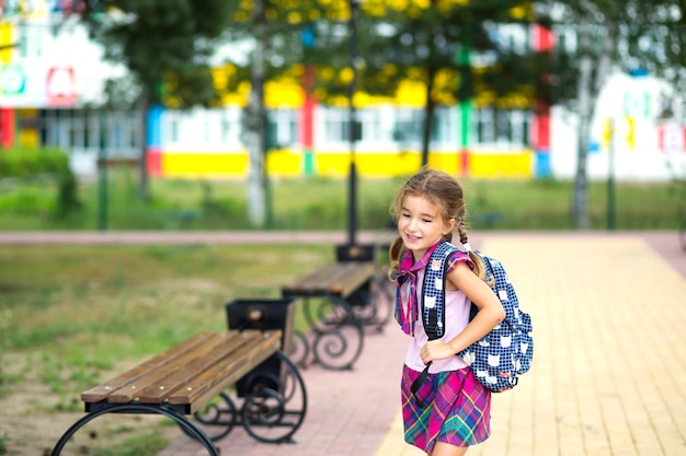 Menina alegre com uma mochila e um uniforme escolar no pátio da escola. De volta às aulas, 1º de setembro. Aluno feliz. Educação primária, classe elementar. Retrato de um estudante