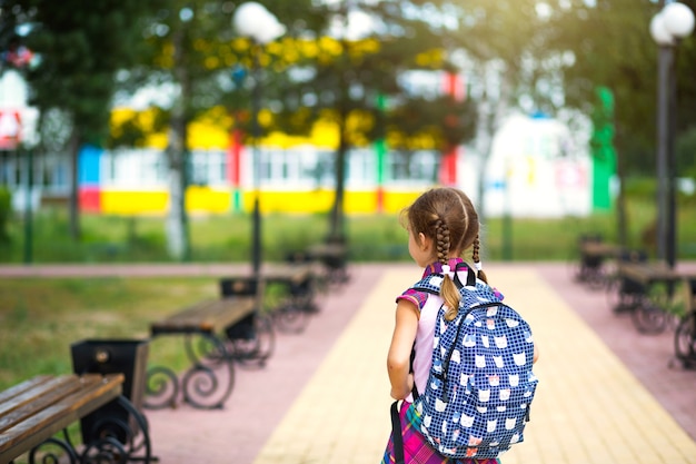 Menina alegre com uma mochila e um uniforme escolar no pátio da escola