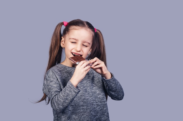 Menina alegre come chocolate e mostra os dentes afetados pela cárie. isolado na superfície cinza