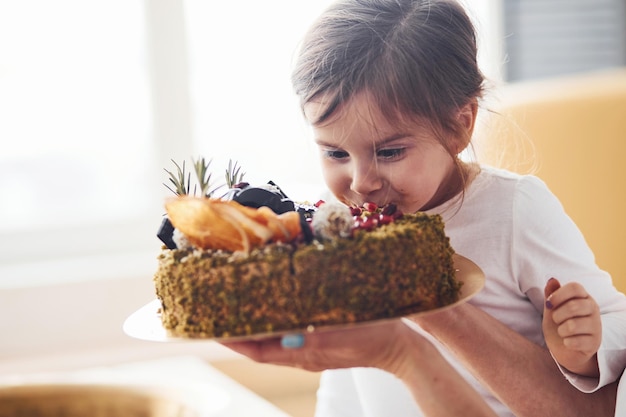 Menina alegre comendo bolo dietético fresco na cozinha