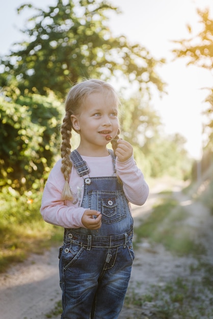 Menina alegre comendo cerejas no jardim no verão. Uma criança come frutas silvestres no jardim.