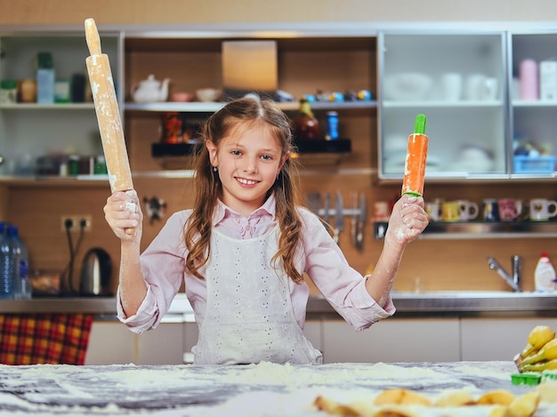 Menina alegre cozinhando massa na cozinha.