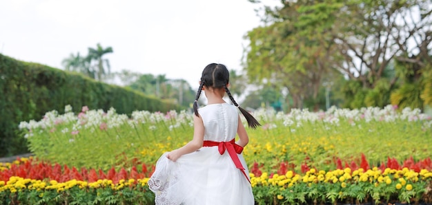 Menina alegre dançando e se divertindo no jardim de flores frescas Criança brincando no parque ao ar livre Vista traseira