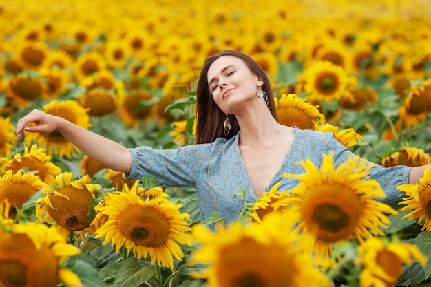 Menina alegre de beleza com girassol, curtindo a natureza e rindo no campo de girassóis ao pôr do sol.