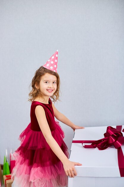 Menina alegre de vestido rosa e chapéu aberto grande caixa de presentes com balões em casa serpentinas de festa de aniversário