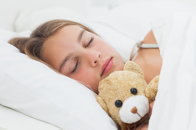 Menina alegre dormindo com seu ursinho de pelúcia