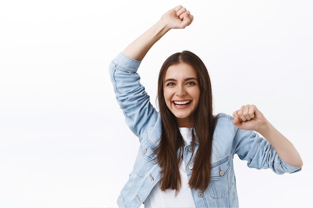 Menina alegre e animada sorrindo alegremente, dançando triunfando como uma competição de equipe vencedora, levante a mão celebrando a vitória, torcendo por um amigo, rindo com alegria, torcendo sobre o fundo branco