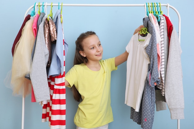 Menina alegre e bonita escolhe roupas com cabides no chão