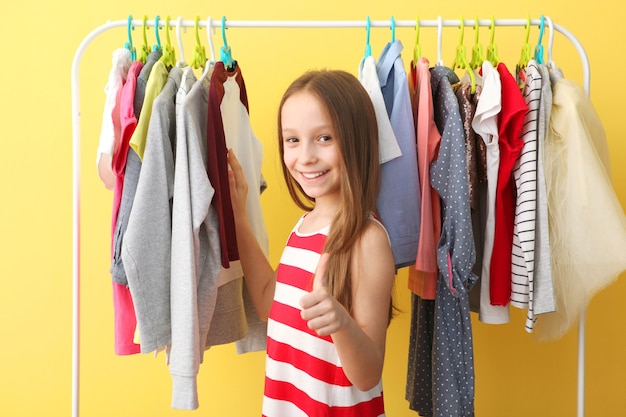 Menina alegre e bonita escolhe roupas com cabides no chão