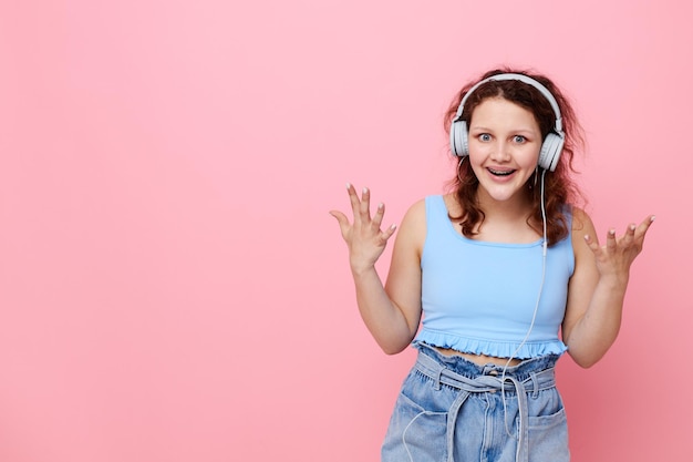Menina alegre em fones de ouvido no estilo juvenil posando fundo rosa inalterado