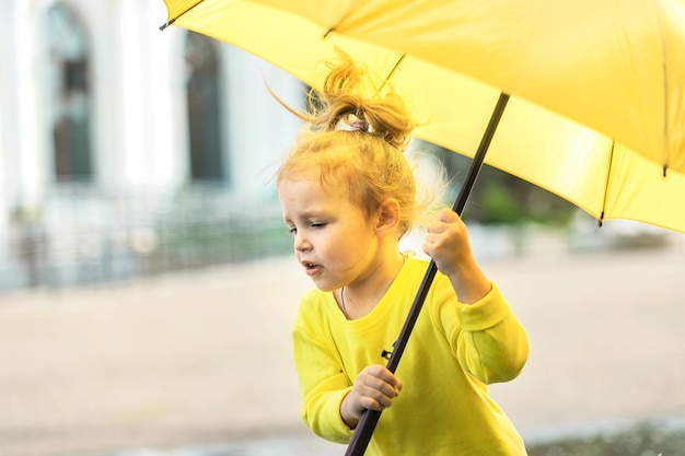 Menina alegre em roupas amarelas tem um guarda-chuva nas mãos em uma rua da cidade depois da chuva