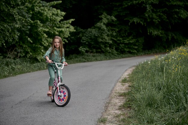 Menina alegre feliz andando de bicicleta no parque na naturezaxD