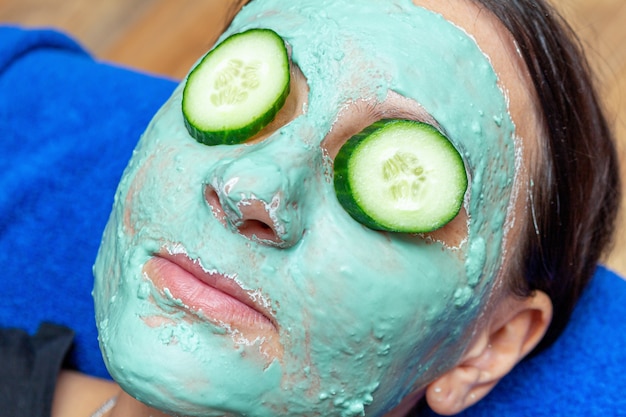 Foto menina alegre feliz com sardas com uma máscara de cosmética verde e fatias de pepino no rosto