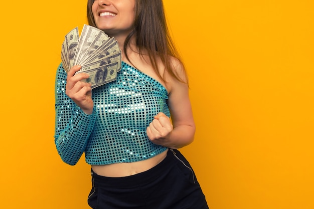 Menina alegre ganhou na loteria e segura um leque de dólares americanos em um fundo amarelo