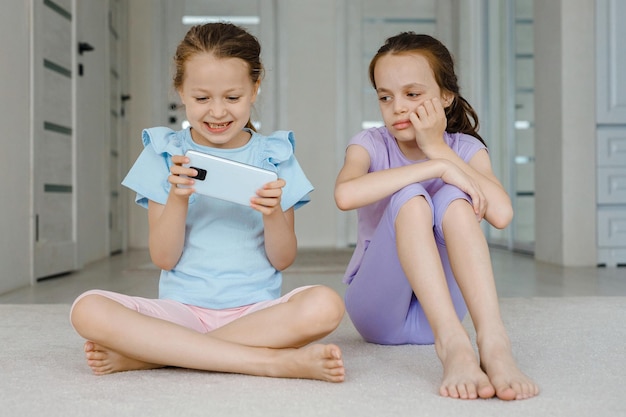 Menina alegre jogando videogame perto da irmã ofendida