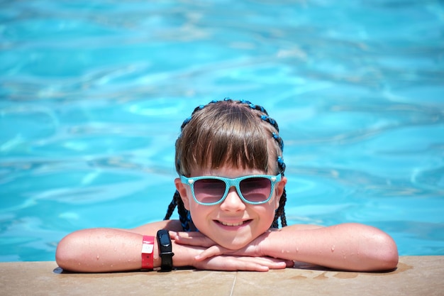 Menina alegre jovem descansando no lado da piscina com água azul clara no dia ensolarado de verão Conceito de férias tropicais