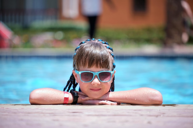 Menina alegre jovem descansando no lado da piscina com água azul clara no dia ensolarado de verão conceito de férias tropicais