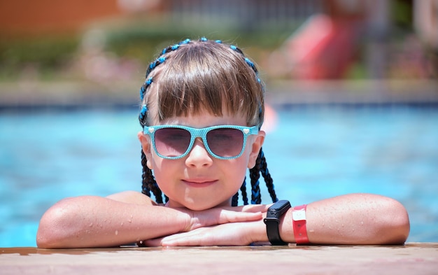 Menina alegre jovem descansando no lado da piscina com água azul clara no dia ensolarado de verão Conceito de férias tropicais