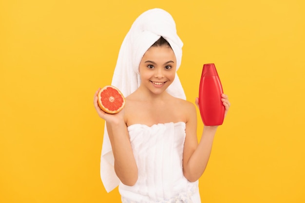 menina alegre na toalha com frasco de xampu de toranja em fundo amarelo.