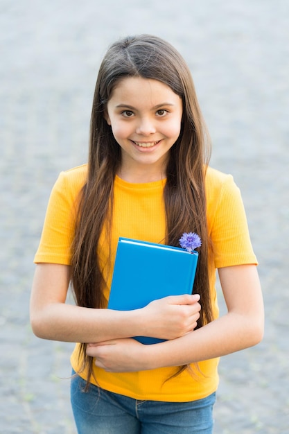 Menina alegre segura o livro de volta à escola criança feliz com educação de notebook para crianças lendo e fazendo anotações desenvolvimento infantil feliz garotinha com diário para memórias