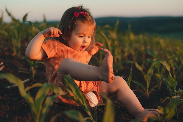 Menina alegre sentada e brincando entre o milharal verde em um dia ensolarado Jardim primavera verão Paisagem natural verão Ambiente rural Linda garota