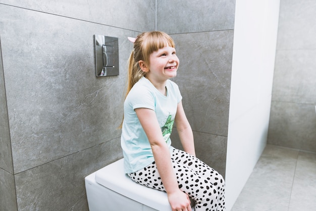 Foto menina alegre sentado no vaso sanitário