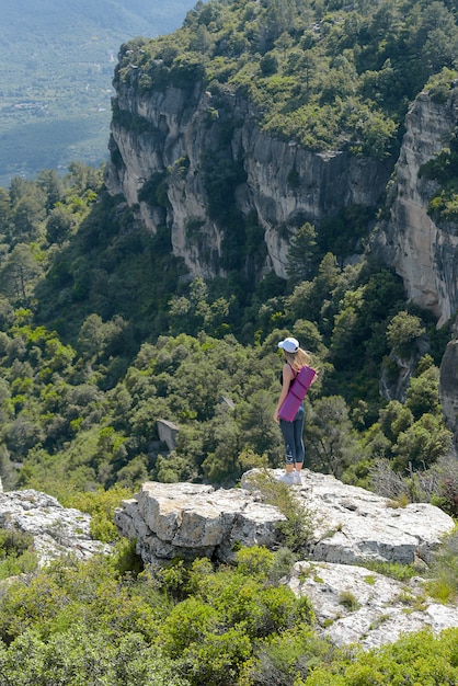 Menina andando com o tapete de ioga na montanha