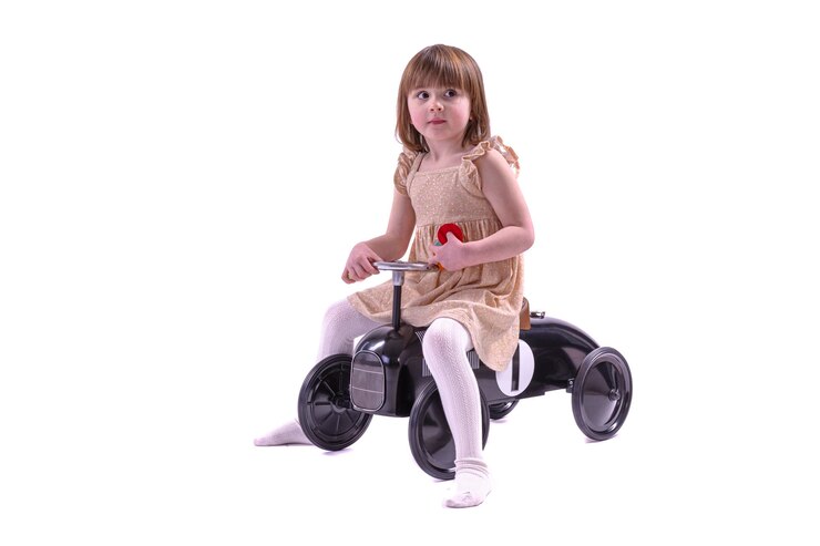 Foto menina andando de carro de brinquedo estilo retro. menina andando de carro de pedais de metal velho para crianças