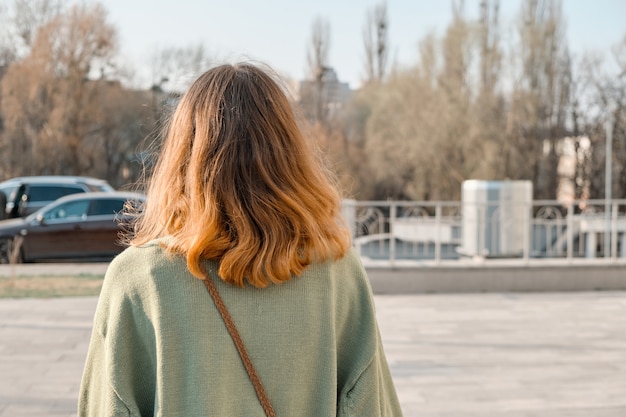 Menina andando de volta com cabelo castanho vermelho na camisola verde