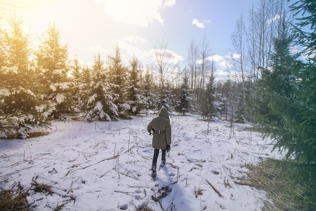 Menina andando na floresta de inverno coberta de neve. Criança explorando a natureza.