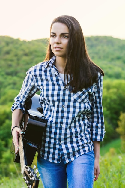 Menina andando no campo com um violão na mão