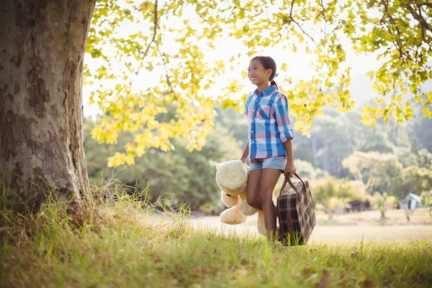Menina andando no parque com uma mala e ursinho de pelúcia